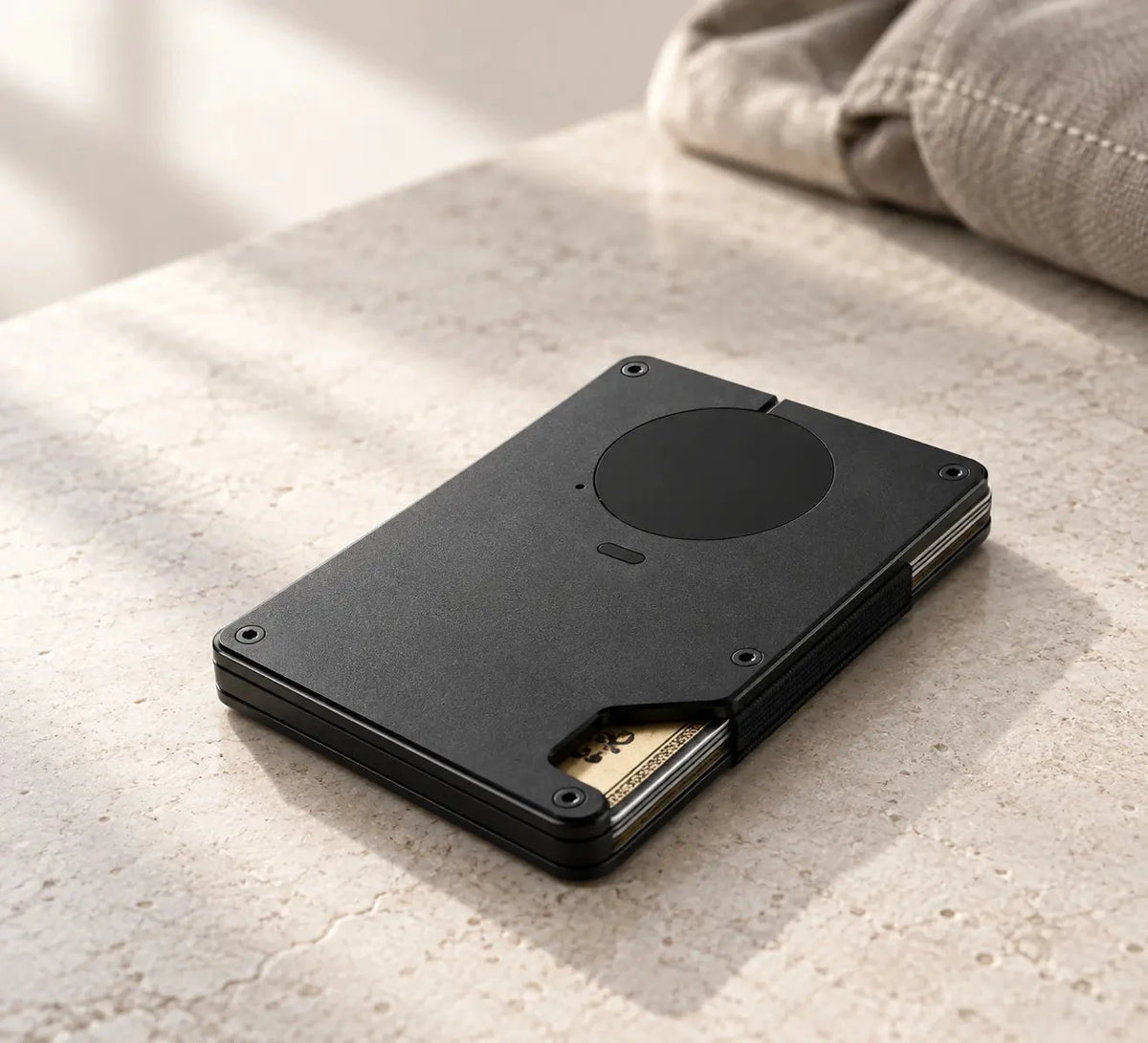 Black metal wallet lying on a stone surface with cards and cash visible at the side.