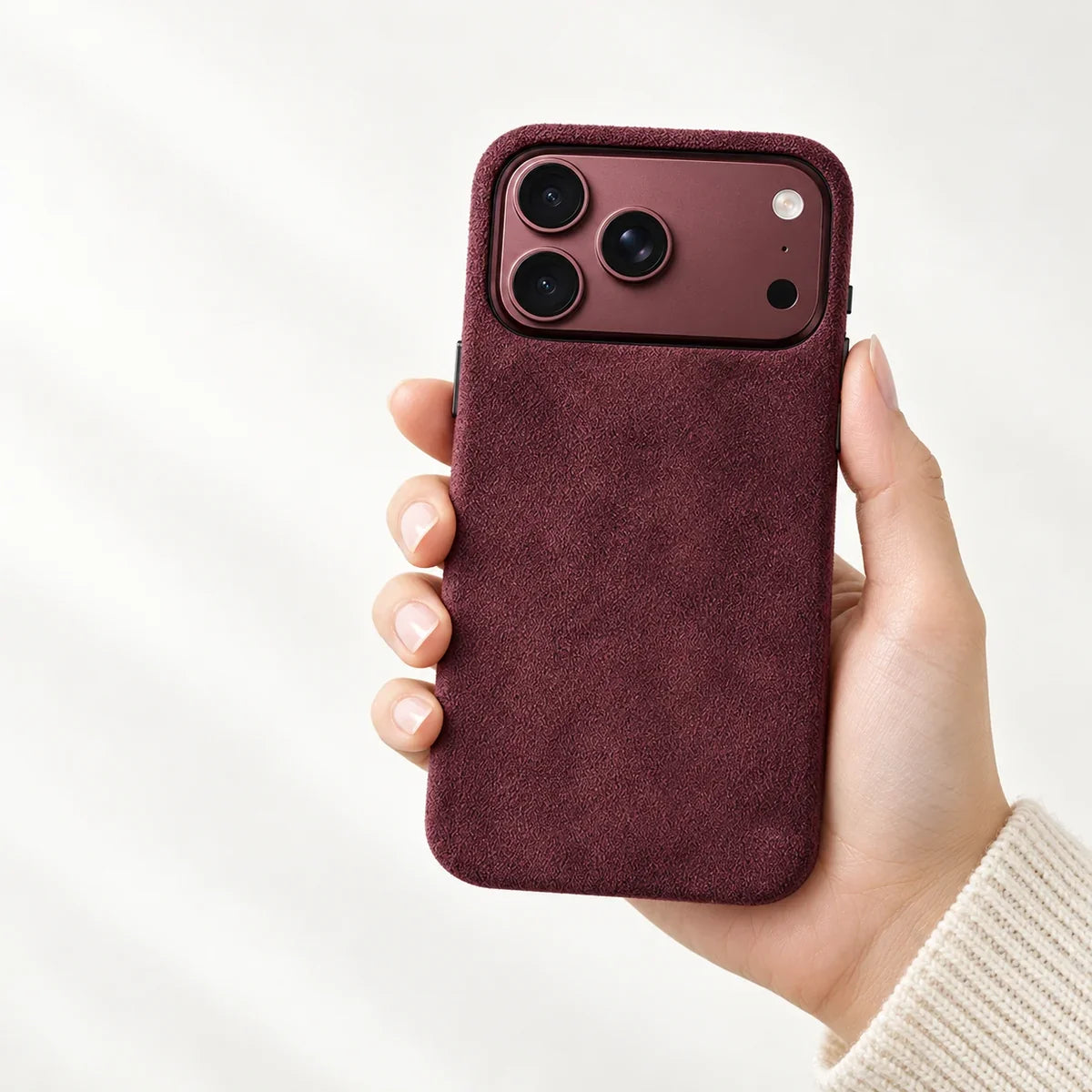 Burgundy fabric phone case held upright in one hand, with a matching Burgundy phone and a wide rear camera opening.