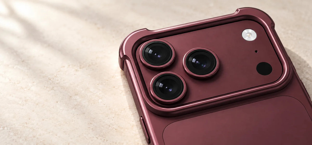 Close-up of a Burgundy aluminum camera guard with raised corners around three rear lenses.