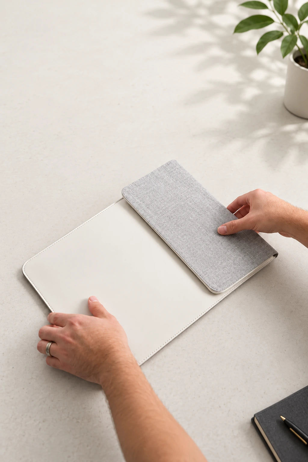 Hands folding the gray fabric flap of a white charging laptop sleeve.